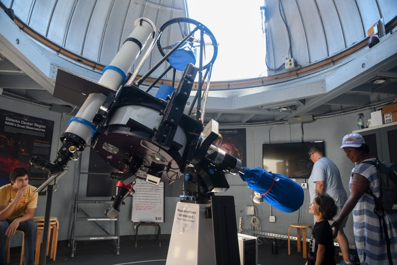 A giant telescope in the foreground with Museum guests and staff at the edges of the image