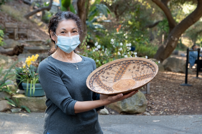 A woman with dark curly hair proudly holds a beautiful basket. She's looking at the camera.